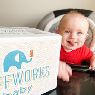smiling boy in high chair with box of Puffworks baby puffs