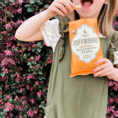 little girl in front of flowering bush eating puffworks original puffs